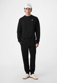 Svart sweatshirt- och byxset i mjukt tyg, med en liten logotyp på bröstet, kombinerat med vita sneakers.
