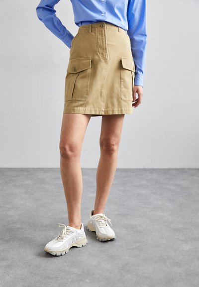 Jupe cargo kaki avec deux poches avant, fermeture à bouton et coupe droite. Associée à des baskets de sport blanches avec des semelles texturées.