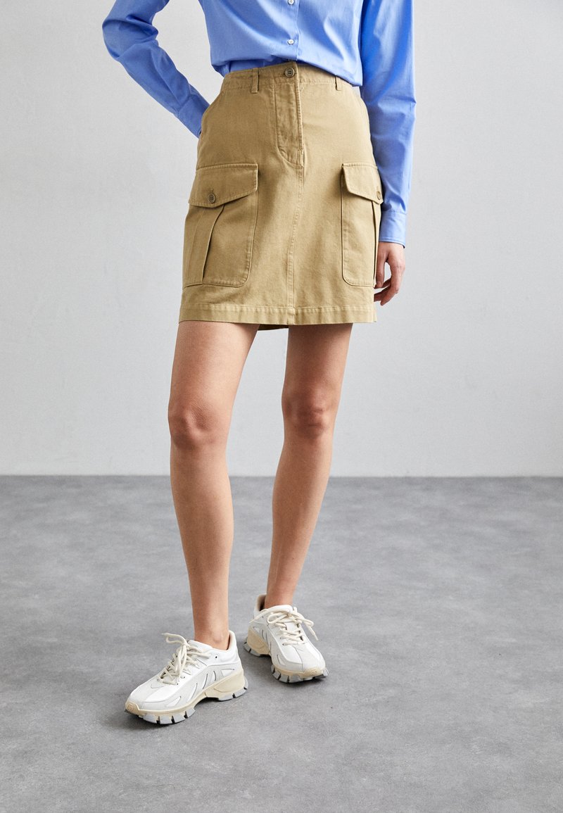 Gonna cargo color khaki con due tasche frontali, chiusura con bottoni e taglio dritto. Abbinata a sneakers sportive bianche con suole testurizzate.