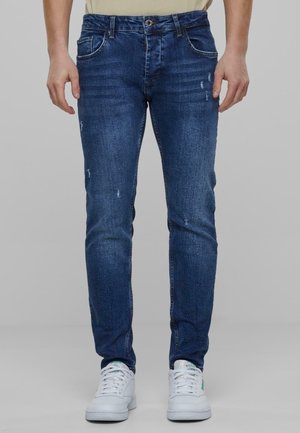 Jeans de mezclilla azul oscuro con ajuste Slim, que presentan detalles desgastados, diseño de cinco bolsillos y cierre de botón en la cintura.