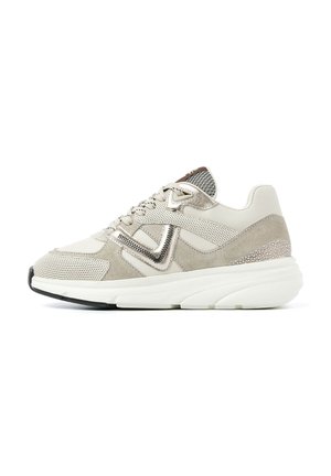 Beige Sneaker, der eine Kombination aus Mesh- und Wildledermaterialien, einer klobigen weißen Sohle, metallischen Akzenten und einem strukturierten Rückenpanel aufweist.