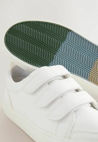 Hvide sneakers med tre velcro-stropper, struktureret læderoverdel og en mønstret gummisål i grønne, blå og brune nuancer.