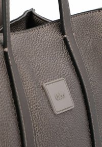 Sac fourre-tout en cuir gris texturé avec deux poignées. Présente une étiquette carrée blanche avec le logo "Gabor". La surface texturée ajoute du détail.