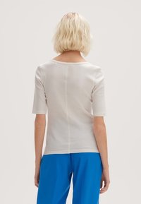 Vit ribbad t-shirt med korta ärmar, rund halsringning och lätt struktur, visad bakifrån, i kombination med blå byxor.