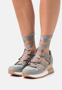 Chaussures compensées grises avec une tige texturée, ornées de rubans satinés croisés autour des chevilles et d'une semelle marron clair contrastante.