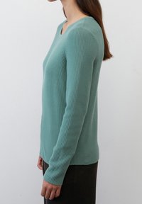Lyse teal strikket sweater med rund halsudskæring, ribbet tekstur og lange ærmer. Sidevisningen viser det tætsiddende design og mid-længde kant.