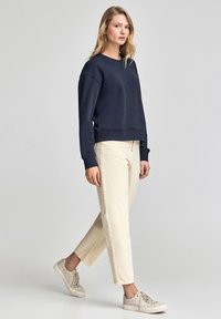 Marinblå sweatshirt med ribbad mudd och nederkant, i kombination med krämfärgade raka byxor och ljusa sneakers. Minimal varumärkesdetalj.