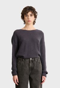 Dunkelgrauer Rippstrickpullover mit weitem Ausschnitt und langen Ärmeln, kombiniert mit hochgeschnittenen schwarzen Jeans. Subtile Textur und lässige Passform.