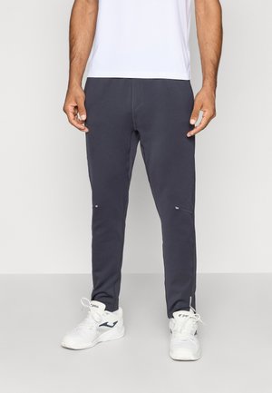 Pantalons de jogging gris foncé en tissu doux avec une taille élastique et des jambes fuselées, dotés de petits accents réfléchissants près des poches.
