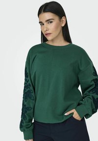 Πράσινο φούτερ από μαλακό μείγμα βαμβακιού, με κεντημένα floral σχέδια σε σκούρο πράσινο στα μανίκια και άνετη εφαρμογή.