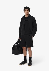 Mustat rento asu, johon kuuluu vetoketjullinen takki, polo-paita ja shortsit. Asusteena musta urheilukassi ja tummat lenkkarit.