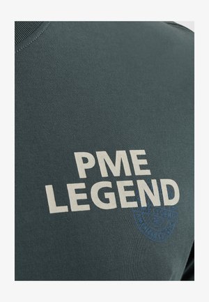 Donkerblauwe t-shirt met ronde hals, featuring vet wit tekst "PME LEGEND" en een blauwe cirkelvormige logo-detail. Zachte, gestructureerde katoenstof.