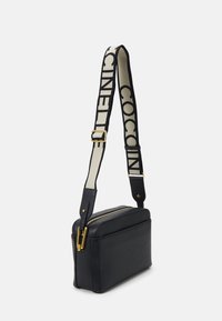 Schwarze Leder-Crossbody-Tasche mit einem goldenen Reißverschluss und einem breiten verstellbaren Tragegurt, der ein schwarzes Logo auf cremefarbenem Hintergrund zeigt, rechteckige Form.