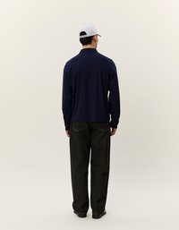 Jūras kara flotes garās piedurknes polo krekls ar apkakli, apvienots ar brīvām tumšo džinsu biksēm un gaišas krāsas cepuri. Minimālisma dizains, bez redzamām ornamentiem.