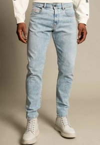 Jeans in denim blu chiaro con vestibilità slim, caratterizzati da un classico design a cinque tasche e una leggera scoloritura. Indossati con sneakers alte bianche.