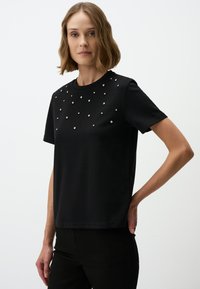 Zwarte T-shirt met korte mouwen van katoen, met een bedelversiering op de voorkant in een verspreid patroon, met een ronde halslijn.