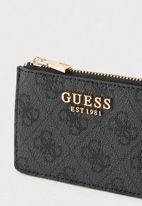 Portafoglio nero con texture, logo "GUESS EST 1981" in tono oro e chiusura con cerniera, caratterizzato da un motivo sottile sul materiale.