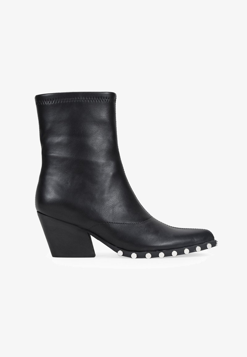 Botín de cuero negro hasta el tobillo con puntera cuadrada, exterior texturizado y tacón grueso. Presenta tachuelas redondas plateadas a lo largo del borde frontal de la suela.