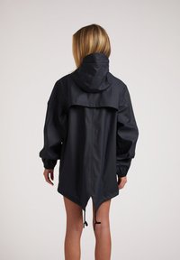 Veste imperméable noire avec une capuche, des manches larges et un ourlet asymétrique. Équipée de cordons de serrage ajustables et d'une texture lisse.