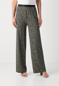 Pantalons larges dotés d'un motif abstrait noir et crème, d'une taille élastique et d'un tissu doux et léger. Accompagnés de chaussures à lanières.