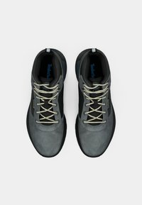 Sudraba un melnbaltas Timberland kedas ar baltām auklām, skatītas no augšas uz baltas fona.