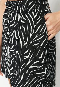 Sort-hvide zebra-stribede shorts med elastisk talje og sidelomme, fremstillet i et tekstureret, letvægtsstof.