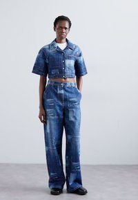 Denimový dvojdielny outfit obsahujúci skrátenú košeľu na gombíky a široké nohavice. Obe kusy majú modrú farbu s potlačou Los Angeles.