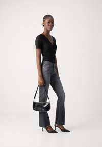 Bodysuit en dentelle noire avec un décolleté en V, jeans gris évasés avec des bords effilochés, et un sac à main noir à motif crocodile. Des escarpins pointus noirs complètent le look.