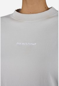Light gray t-shirt made of soft, lightweight fabric. Features a ribbed neckline and stitched white text "PEGADOR" on the chest.