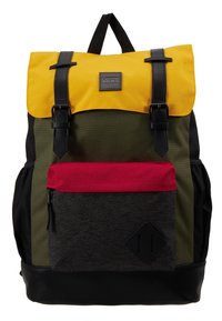 Sac à dos avec rabat supérieur jaune, corps vert olive, fond noir, poche avant rouge, bretelles en cuir noir et écusson logo Vans sur le rabat.