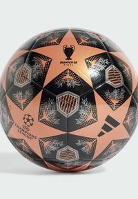 Balón de fútbol Adidas en negro y naranja con formas de estrellas, patrones decorativos y el logo de la UEFA Champions League. Texto "Final de Múnich 25".