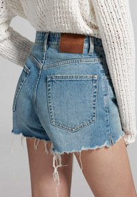 Hellblaue Denim-Shorts mit ausgefranstem Saum und zerrissenen Details, ausgestattet mit zwei Gesäßtaschen und einem braunen Leder-Label.