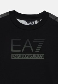 T-shirt noir en coton avec un logo EA7 en gris bien visible, col rond et accents d'épaules à motifs contrastants.