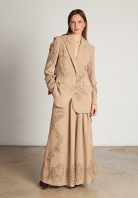 Blazer beige ajustado y falda a juego, con bordados florales en relieve en las mangas y el dobladillo, y una textura de tela suave.