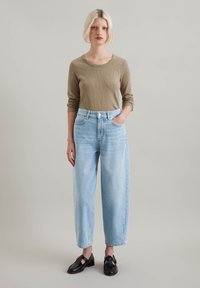 Light brown long-sleeve top paired with high-waisted, light blue wide-leg jeans. Features a classic fit and subtle detailing on pockets.
