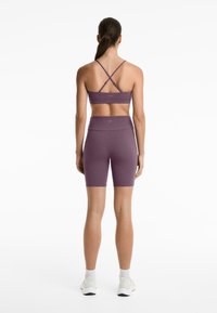 Lila idrottsbralette med korsade band och matchande högmidjade shorts. Slitstift, stretchigt tyg, minimal varumärkesprofil och åtsittande design.