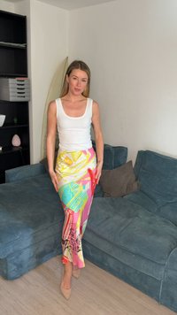 Femme en débardeur blanc et jupe colorée debout à côté d'un canapé d'angle en velours côtelé bleu dans un salon.