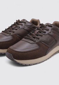 Zapatillas marrones con una combinación de cuero liso y ante texturizado. Presentan un diseño con cordones, suela de goma y una marca mínima en el lateral.