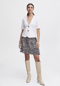 Hvid kortærmet blazer med V-udskæring og to sorte knapper, parret med en beige leopardprint nederdel og beige støvler til knæet.