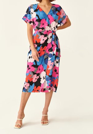 Kvinde iført en knælængde omslagskjole med korte ærmer og et lyst blomsterprint i pink, blå, rød og sort.