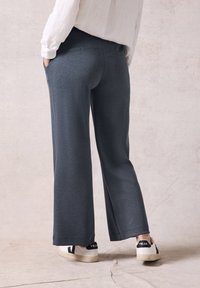 Helle Stoffhose in Dunkelgrau mit glatter Textur, seitlichen Taschen und lockerer Passform, kombiniert mit weißen Sneakers.