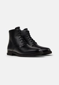 Botas de cuero negro hasta el tobillo con un acabado liso, punta redonda y diseño de cordones. Cuentan con un tacón bajo apilado y una suela resistente.