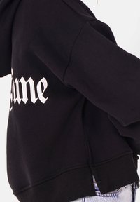 Svart sweatshirt med vit broderad "Fortune"-text på vänster ärm. Tillverkad av mjukt material med en avslappnad passform och ribbade muddar.