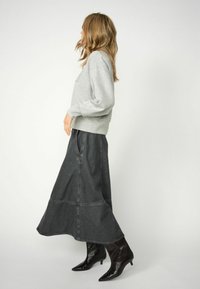 Hallideh grey sweatshirt pikkade käistega, millele on sobitatud tume denimpahiks, millel on laienev äär, ja mustad läikivad pahkluusaapad.