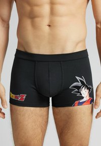 Svarta boxer shorts i elastisk tyg med en tryckt grafik av en karaktär på vänster sida och en logotyp på framsidan.