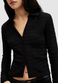 Cardigan nero texturizzato con un motivo ondulato, maniche lunghe, colletto e chiusura con bottoni; aderisce al corpo.