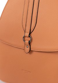 Borsa in pelle color tan con una superficie liscia, dotata di una tracolla cucita in nero e accessori metallici, tra cui un dettaglio con chiusura circolare.