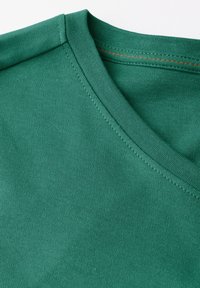 Zelené tričko s výstřihem do V vyrobené z měkké bavlněné tkaniny. Má hladkou texturu a pečlivě šité švy, což ukazuje na jednoduchý design.