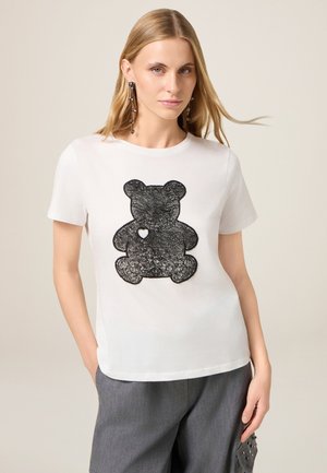 Witte katoenen t-shirt met een zwart teddybeerontwerp en een hartdetail. Korte mouwen en een relaxte pasvorm.