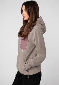 Lichtgrijze fleece hoodie met een kastanjebruine borstzak. Voorzien van een ritsluiting, zijzakken en een zachte textuur. Met capuchon.